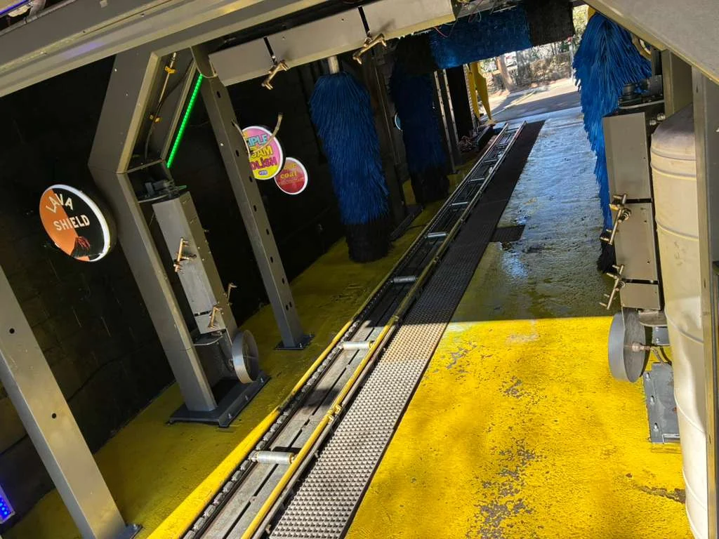 View down a tunnel lane, with the conveyor track, steel arches and blue brushes over a yellow floor